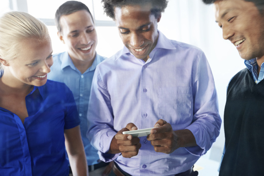 A group of happy business people all looking at a smart phone together